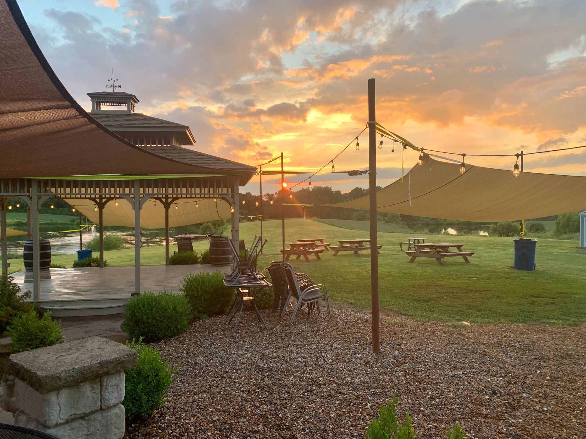 Sunset over a gazebo, outdoor seating, and a grassy field. Evening sky is orange and yellow.