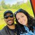 Smiling couple in sunglasses on a cable car; greenery in background.