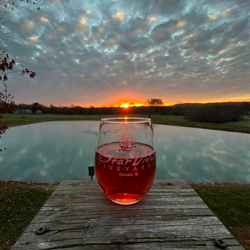 Glass of red wine in front of a sunset over a pond at Star View Vineyard.