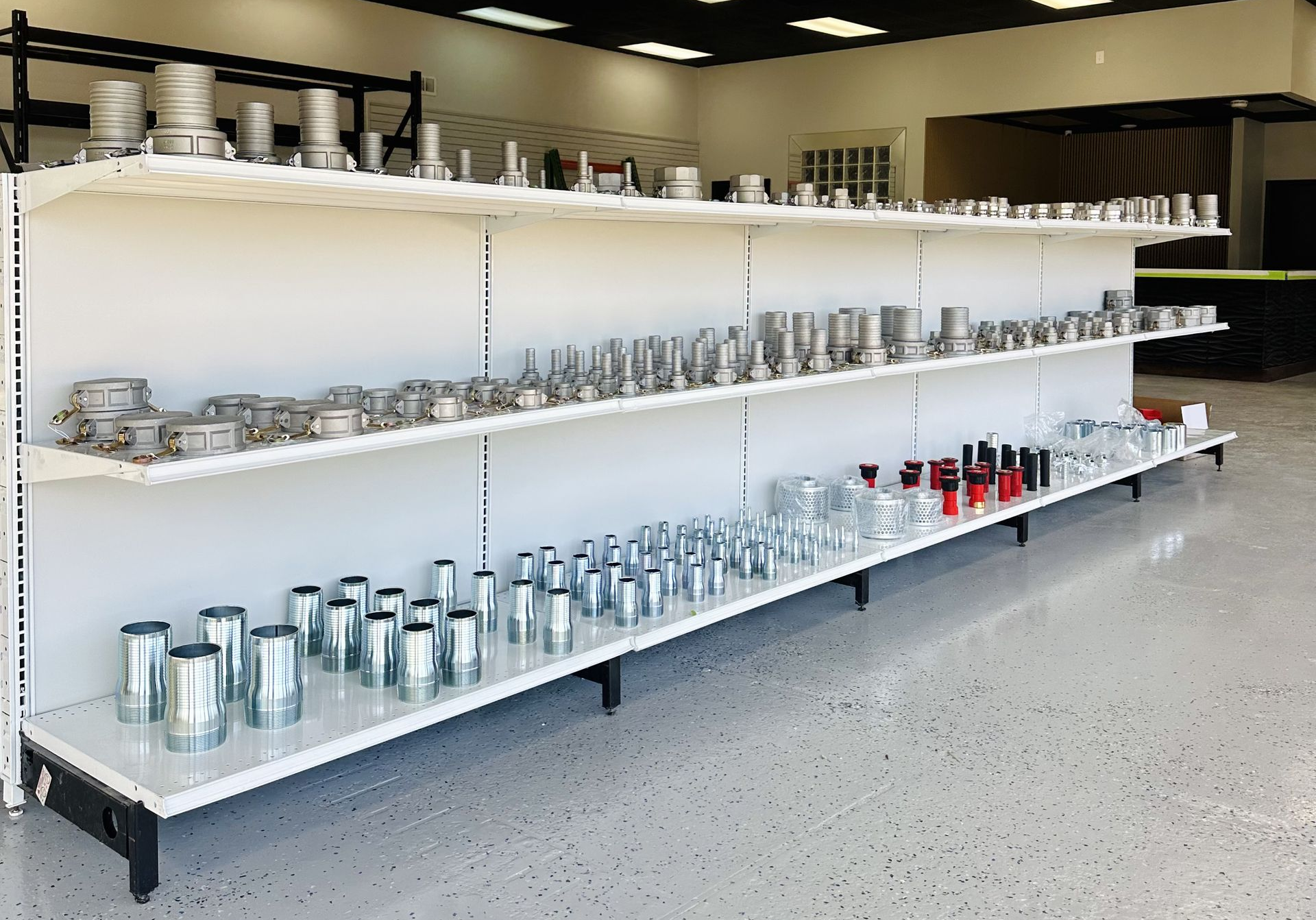 Rows of shiny metal containers and tools on white shelves in a bright workshop or storage room