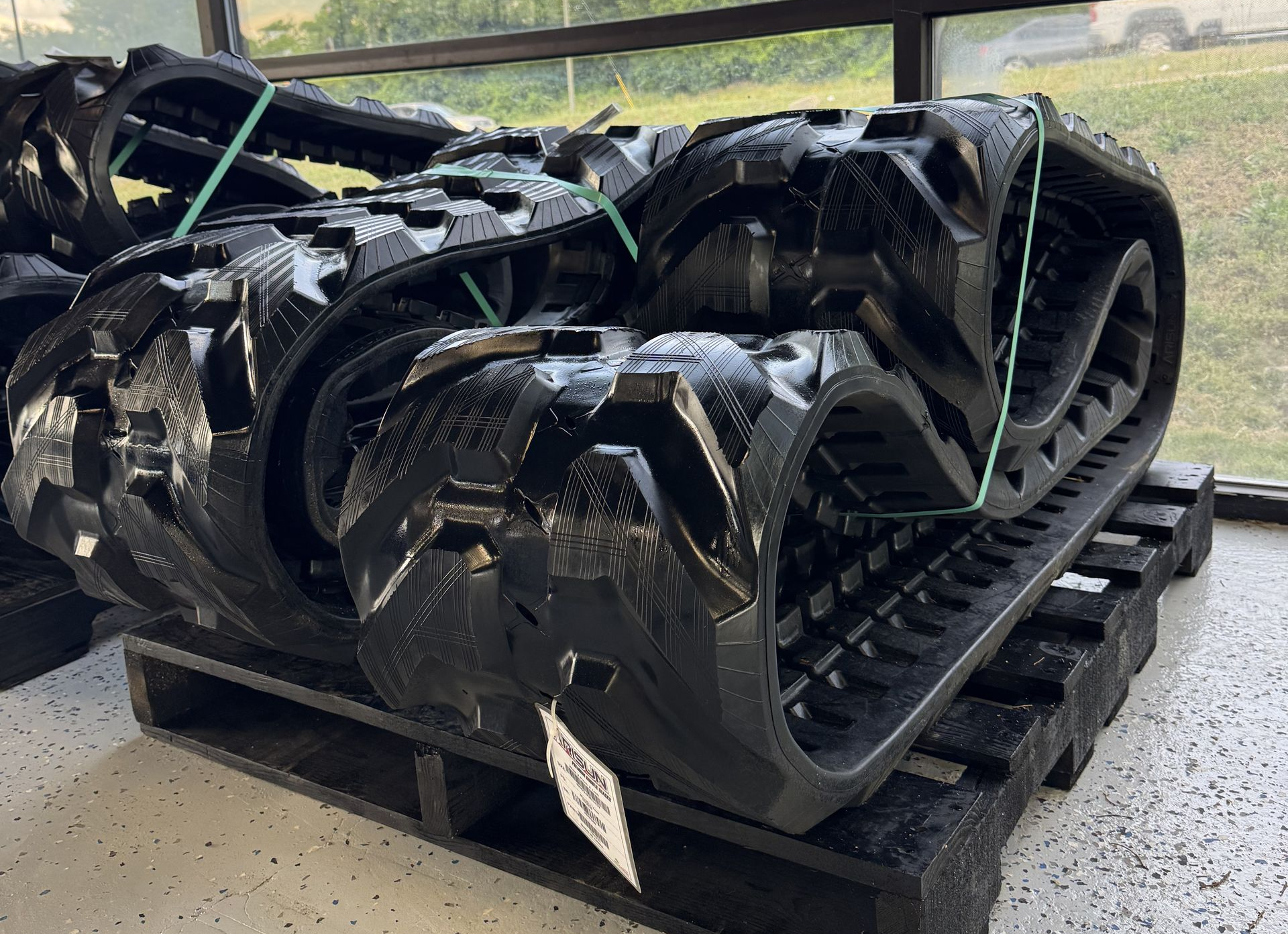 Black tracked all-terrain vehicle treads strapped on a pallet in a garage.