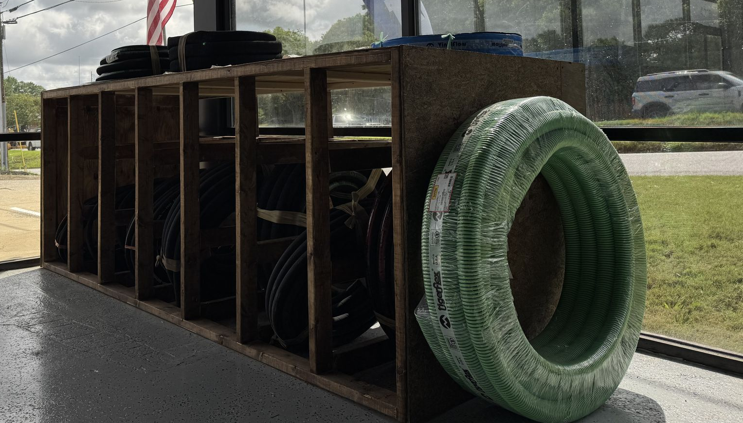 A large wooden playground tunnel with a green tire on the end, sitting outdoors on pavement.
