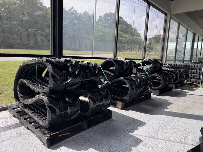 Rows of large black industrial machinery parts on pallets beside a long windowed wall.