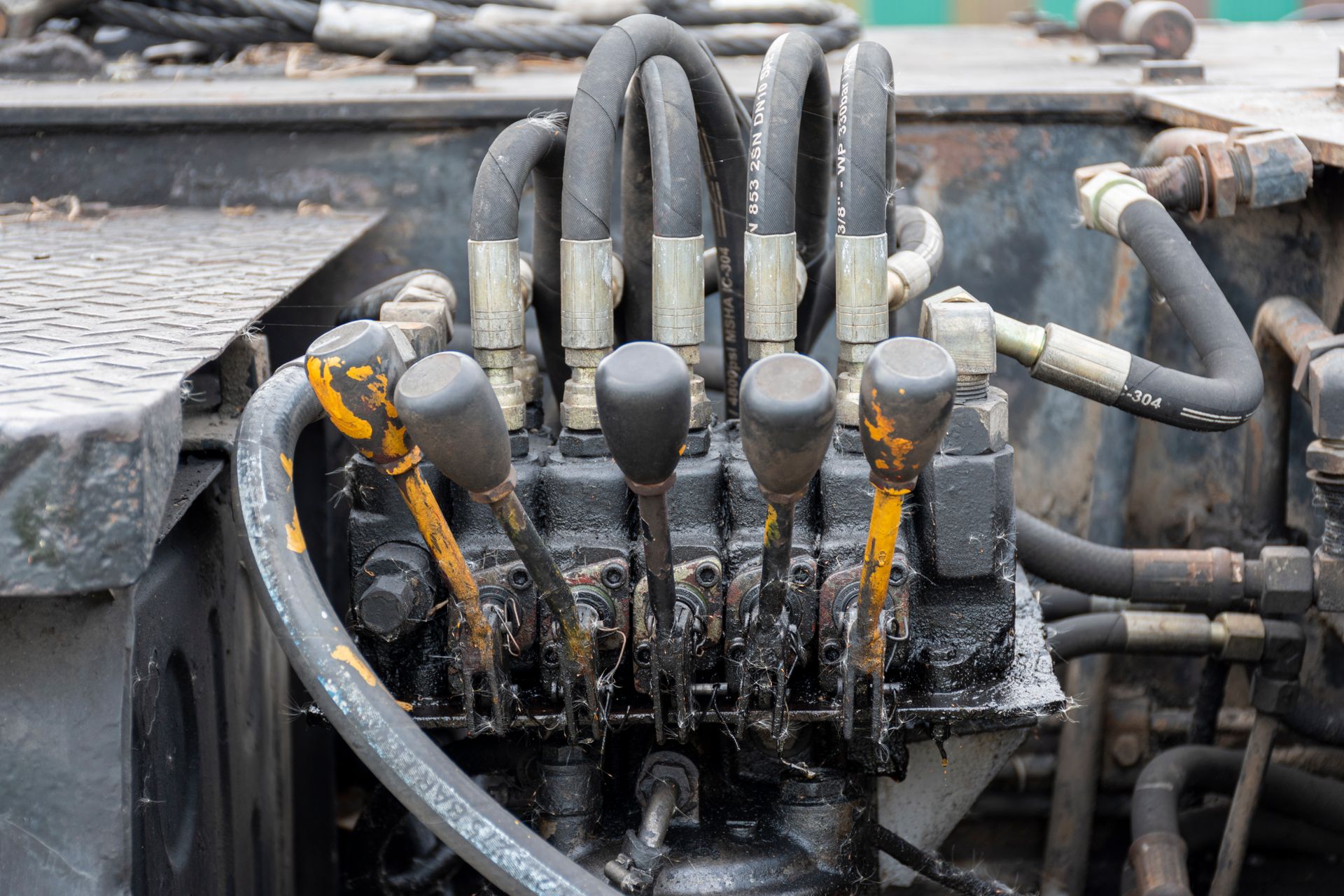 Close-up of a muddy hydraulic valve manifold with black hoses and yellow paint marks on industrial machinery