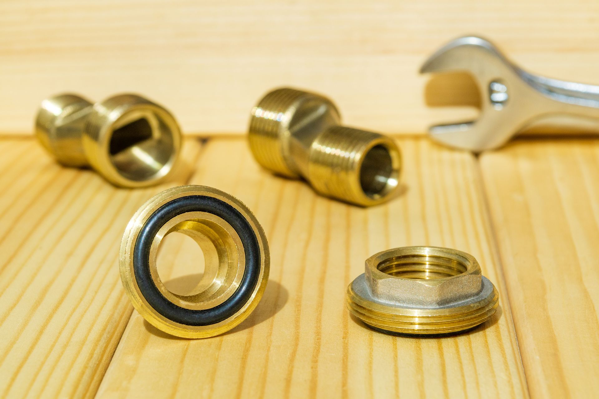Assorted brass plumbing fittings and a wrench on a wooden surface