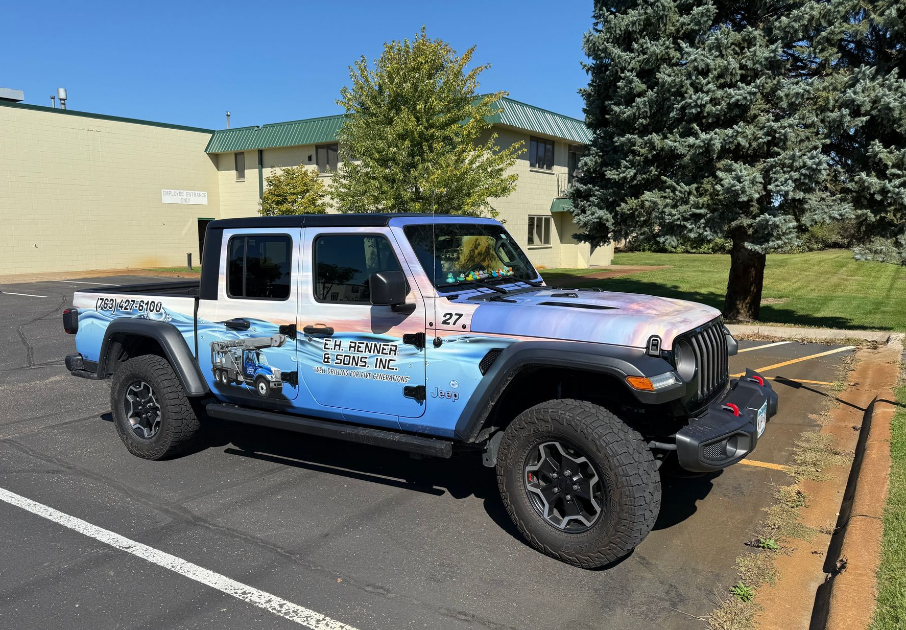 Blue Jeep Gladiator pickup truck with graphics, parked in a lot, sunny day.
