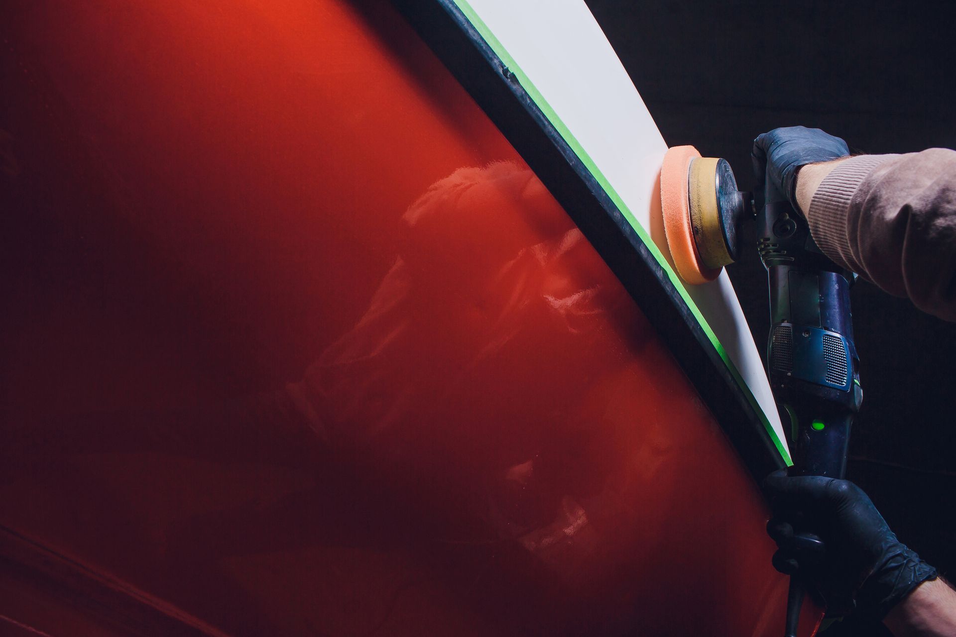 Person polishing a red car with an electric buffer in a dark garage.