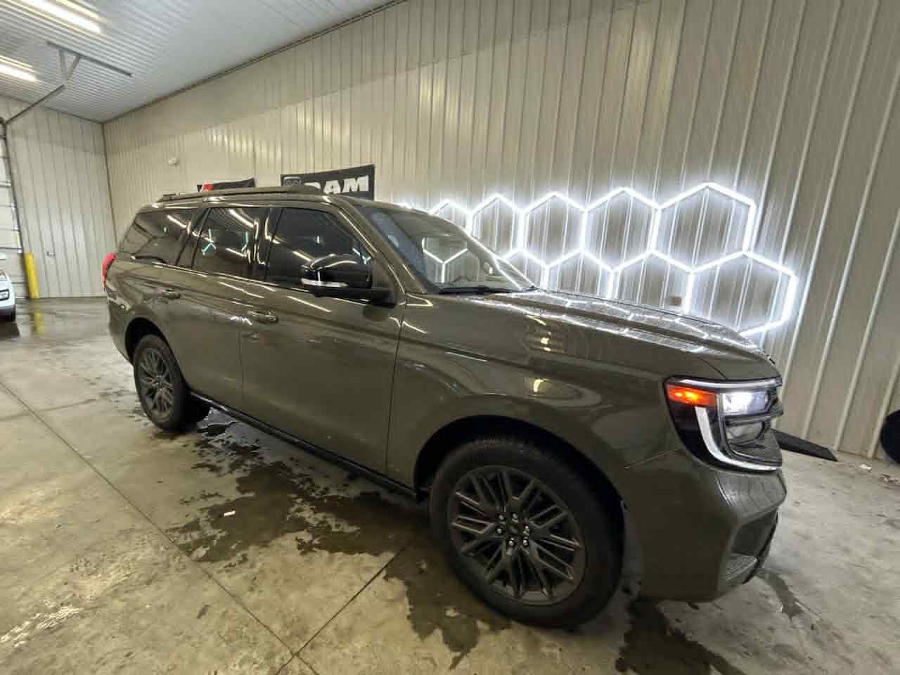 A dark gray SUV parked in a garage with black wheels. White, hexagonal lights are on the wall.