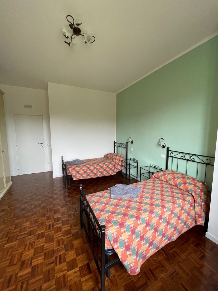 Camera da letto con due letti singoli; pavimento in legno, parete con dettagli verdi, porta bianca.