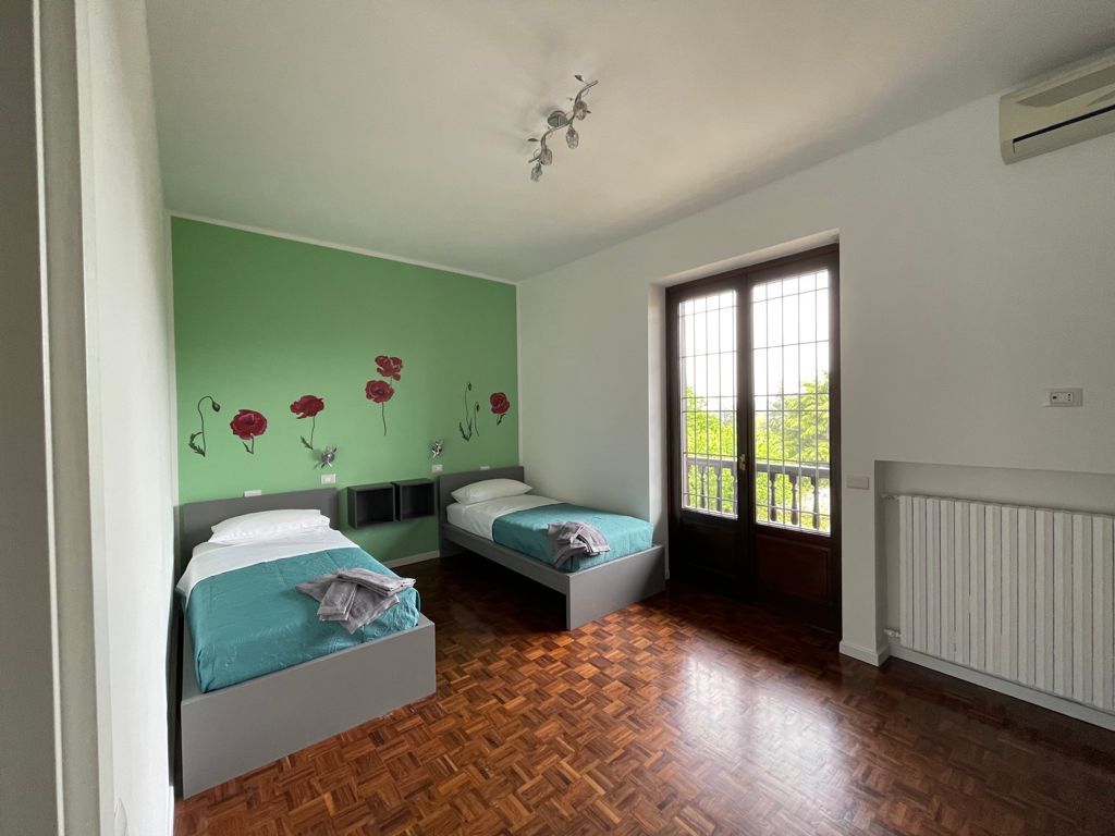 Camera da letto con due letti singoli, parete verde con decalcomanie floreali e porta-finestra.