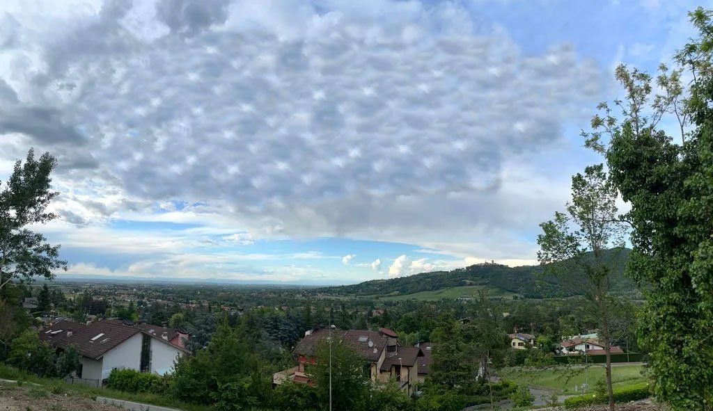 Vista su una valle con un paesaggio urbano, sotto un cielo nuvoloso drammatico, alberi in primo piano.