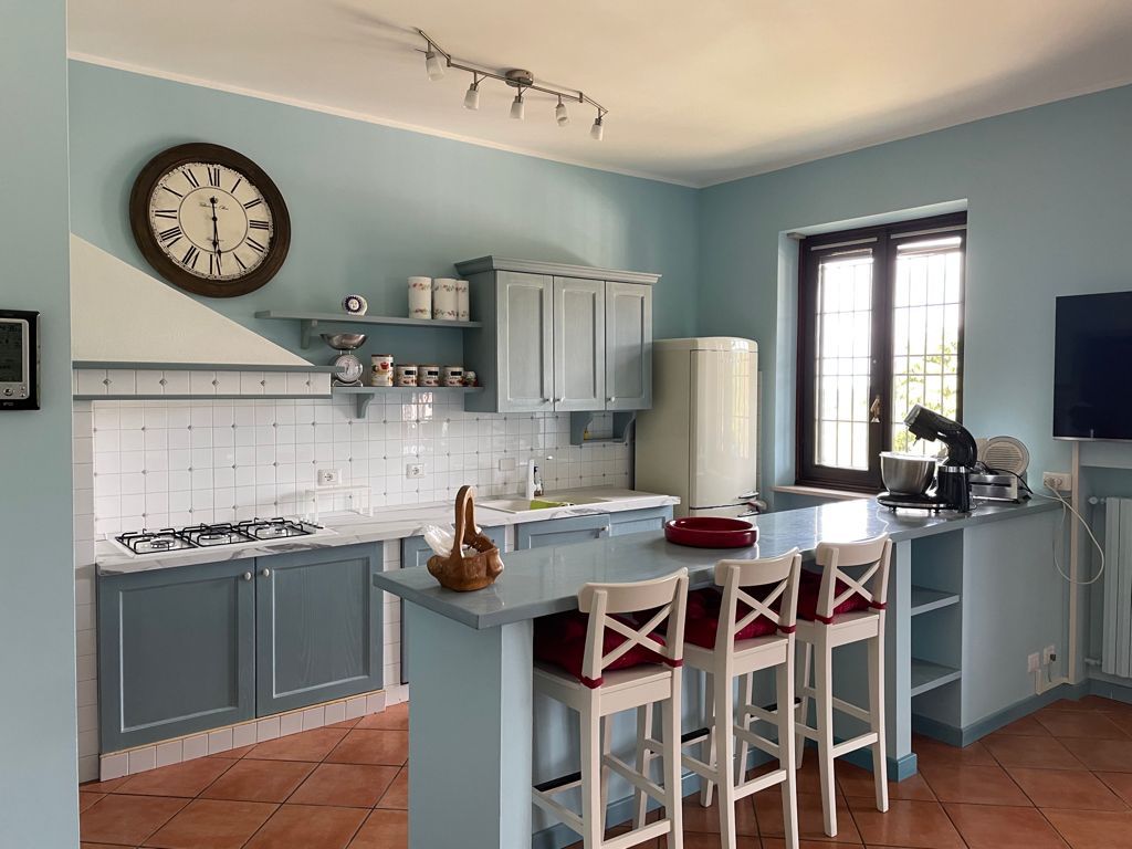 Cucina blu con isola e sgabelli da bar, orologio, fornello, mobili e finestra.