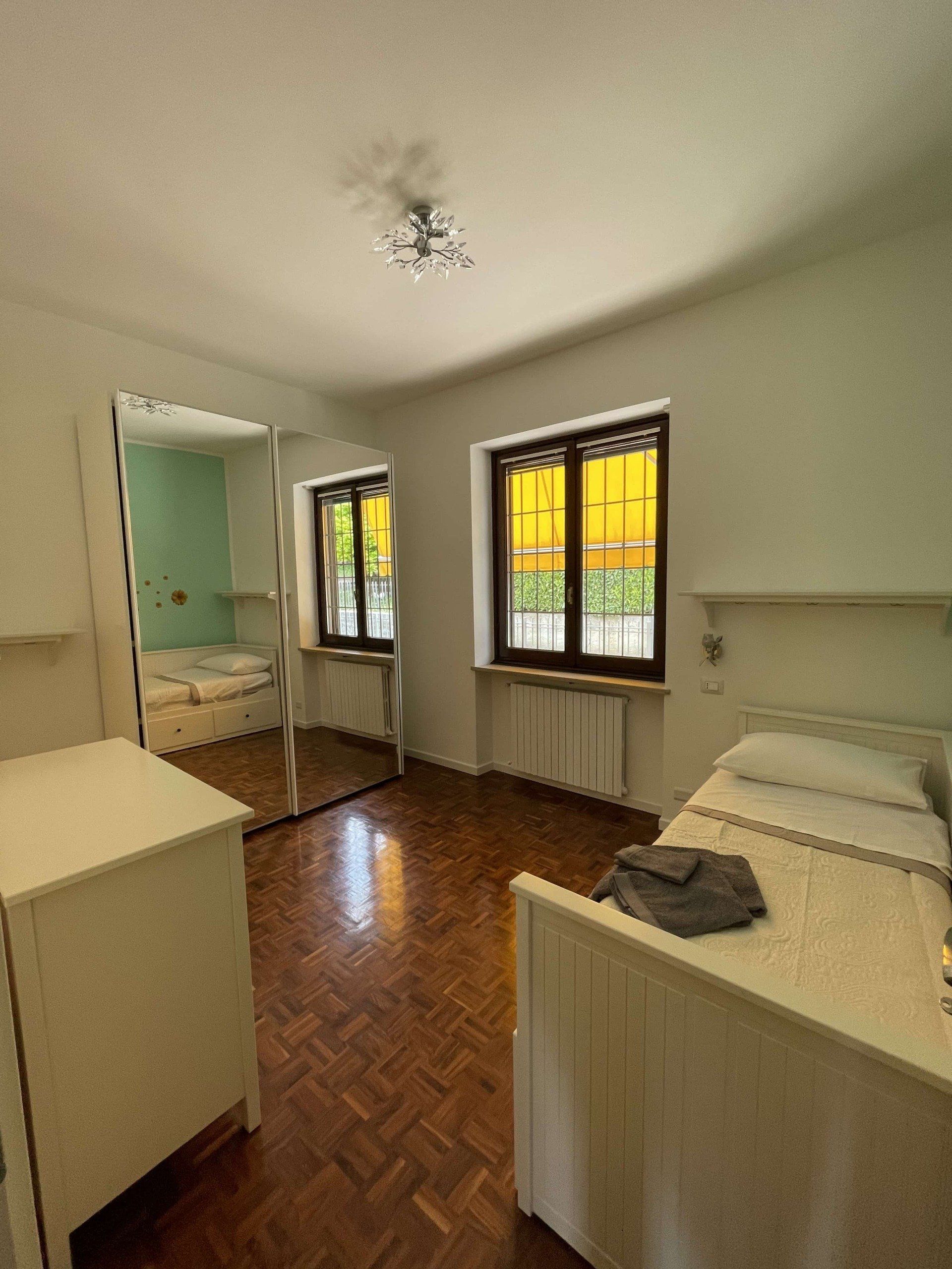 Camera da letto con armadio a specchio, due letti e pavimento in legno.