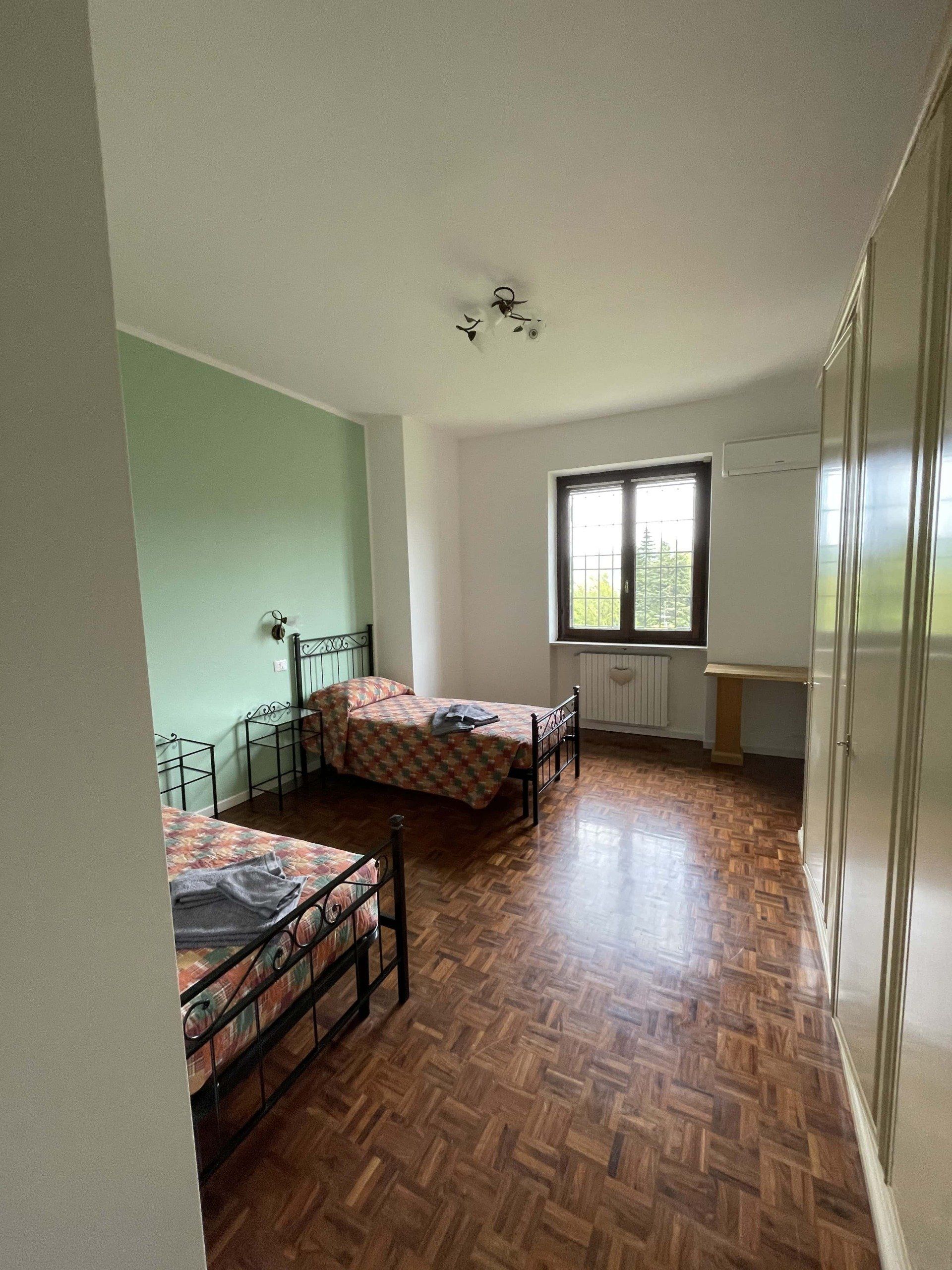 Due letti singoli in una camera da letto con pavimenti in legno, una finestra e una parete decorata con elementi verdi.