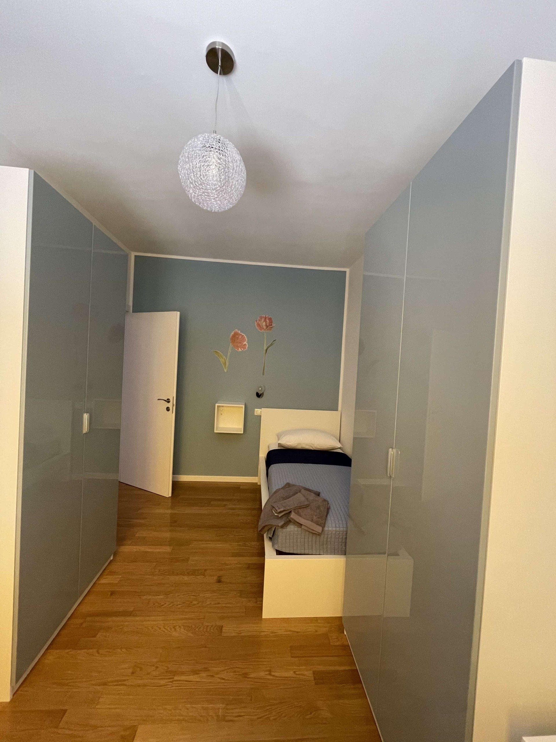 Camera da letto stretta con pareti azzurre, pavimento in legno e un letto.