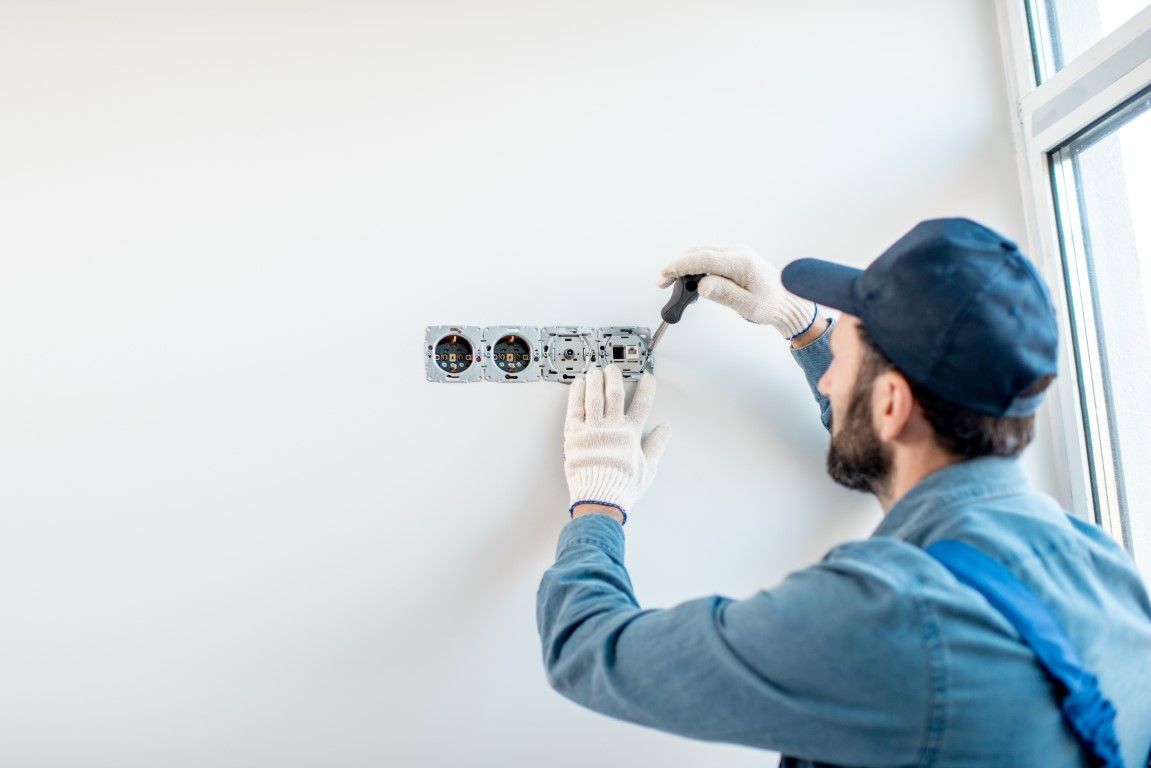 Electrician installing wiring in a wall outlet box indoors