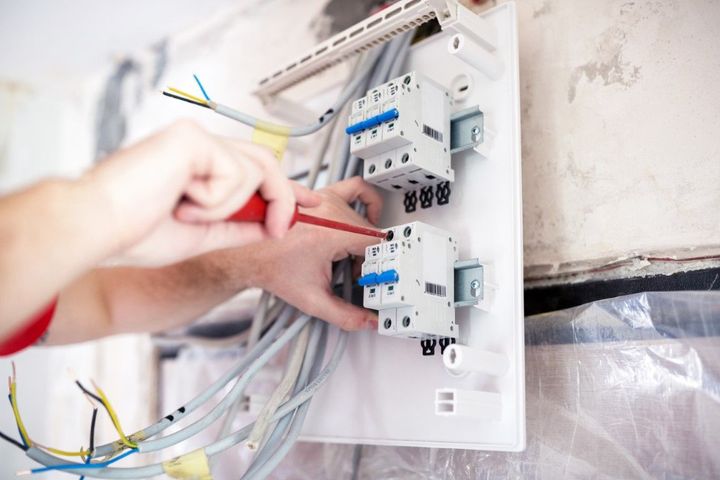 Hands wiring an electrical breaker panel with blue switches and exposed cables