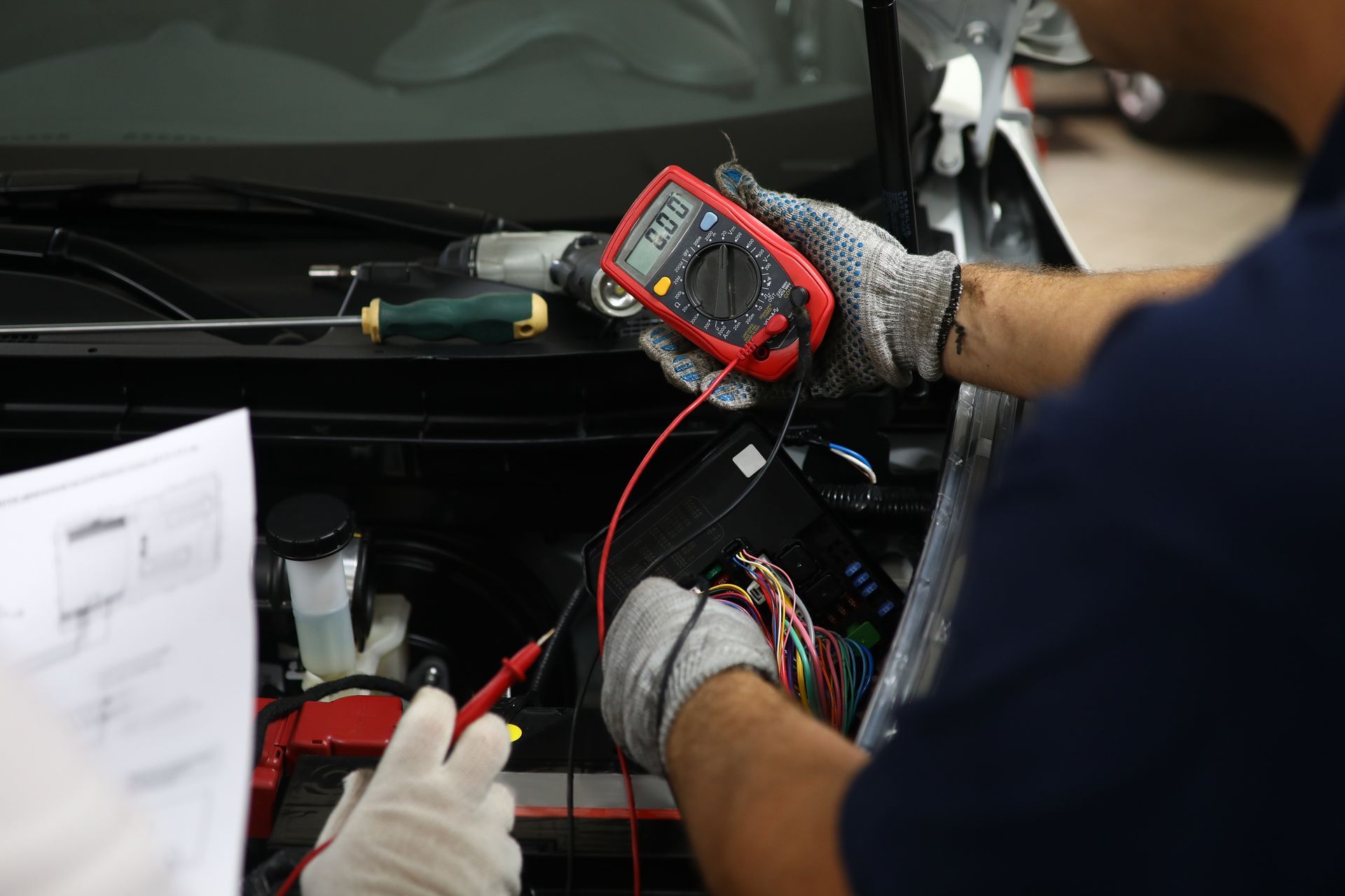 Mechanic performing automotive repair using multimeter to test vehicle wiring and electrical system.