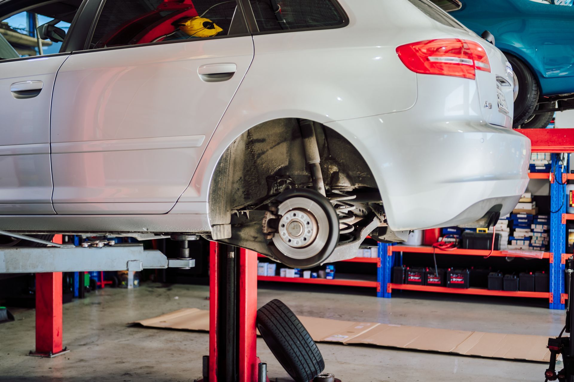 A silver car is raised on a lift in an auto repair shop, with a tire removed for brake work.