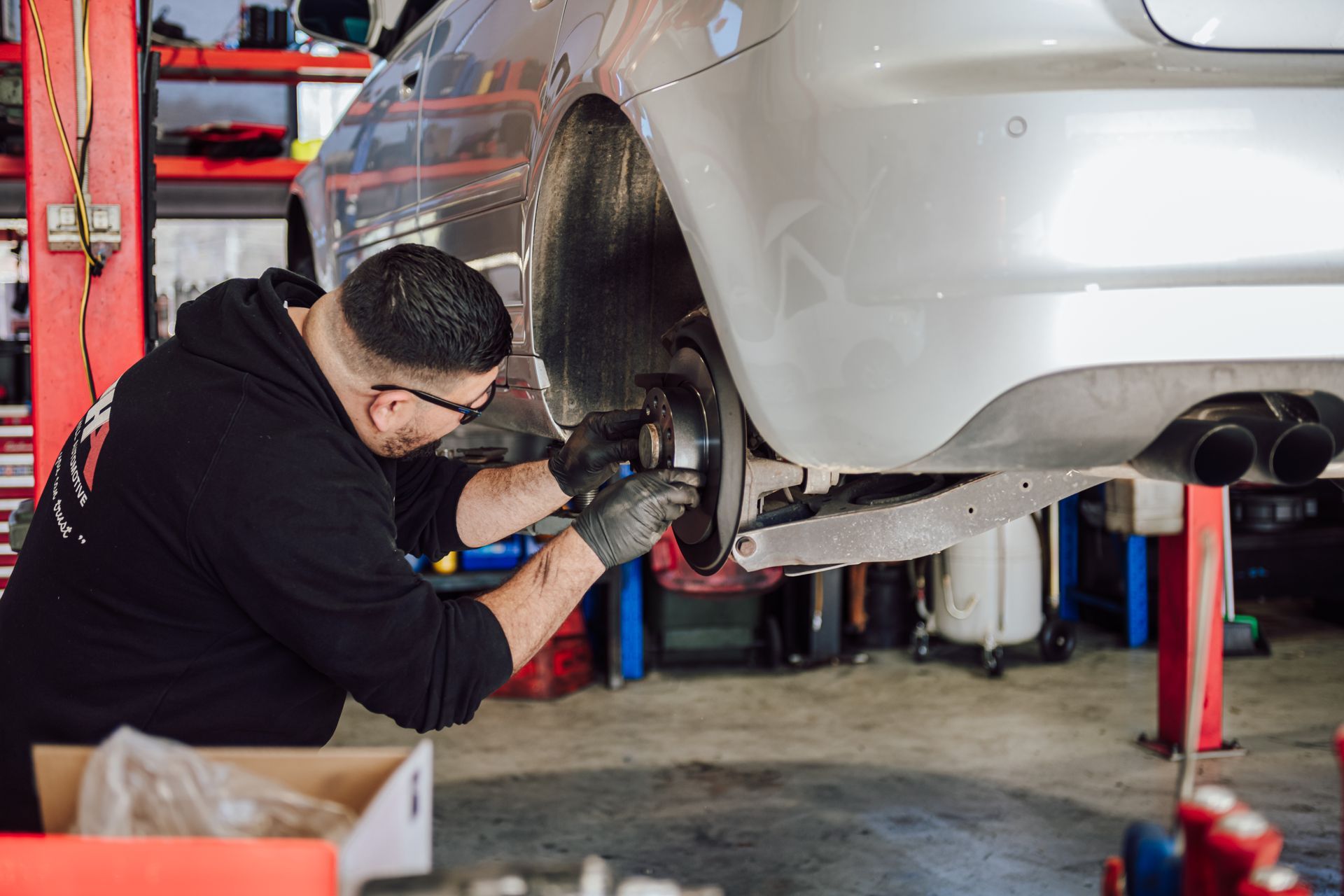 Mechanic in black clothing working on car brake in a repair shop.