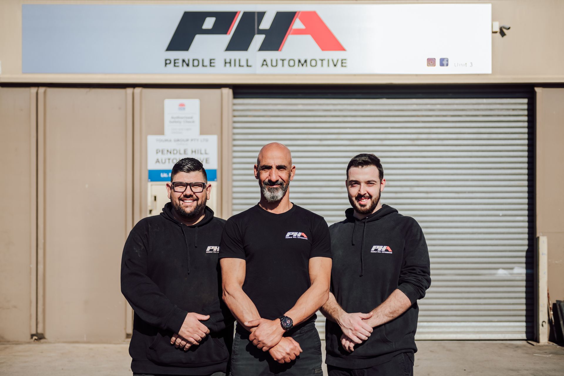 Three men in front of Pendle Hill Automotive. They are wearing black shirts and smiling.