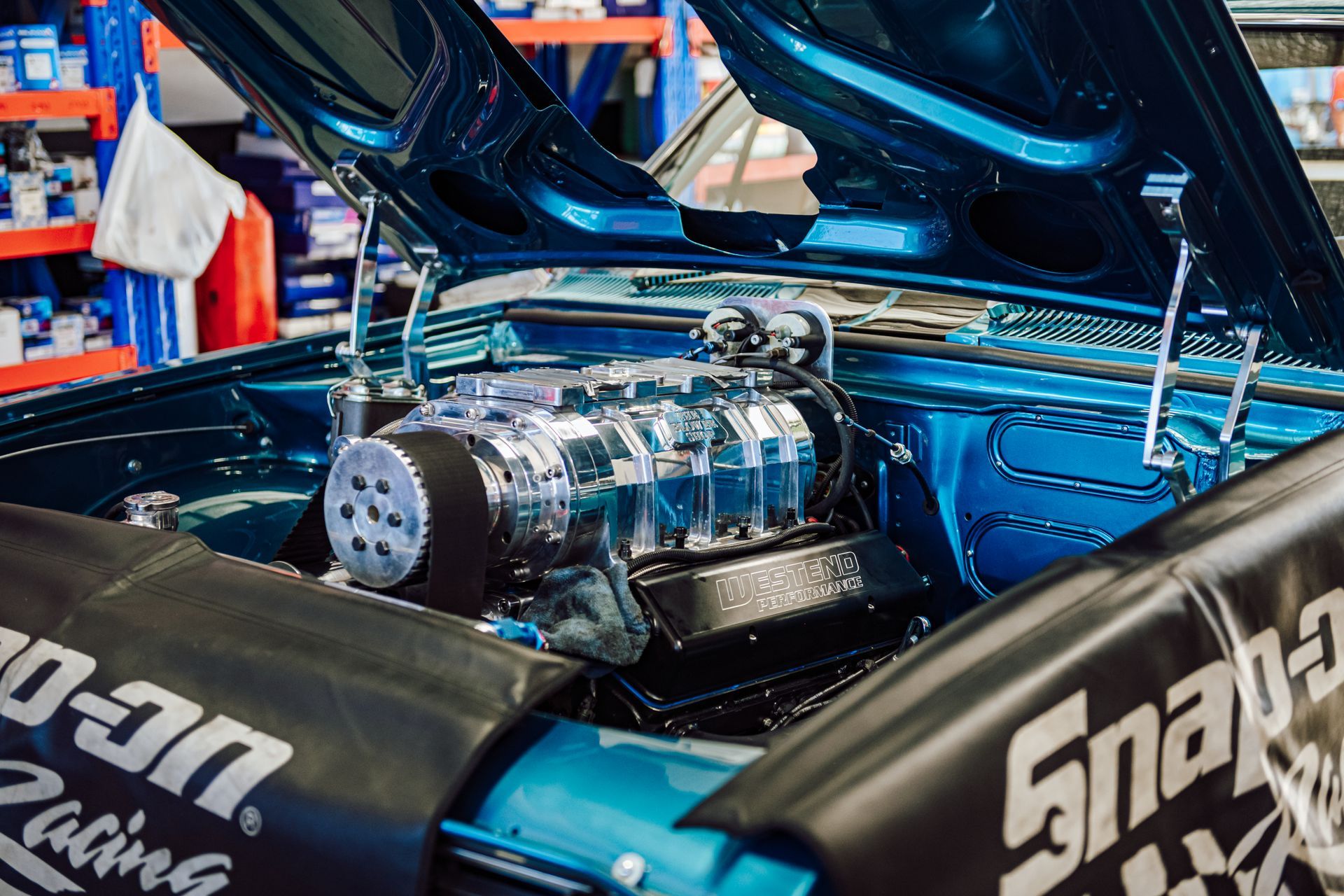Blue vintage car engine with chrome supercharger, Snap-on Racing cover in garage.
