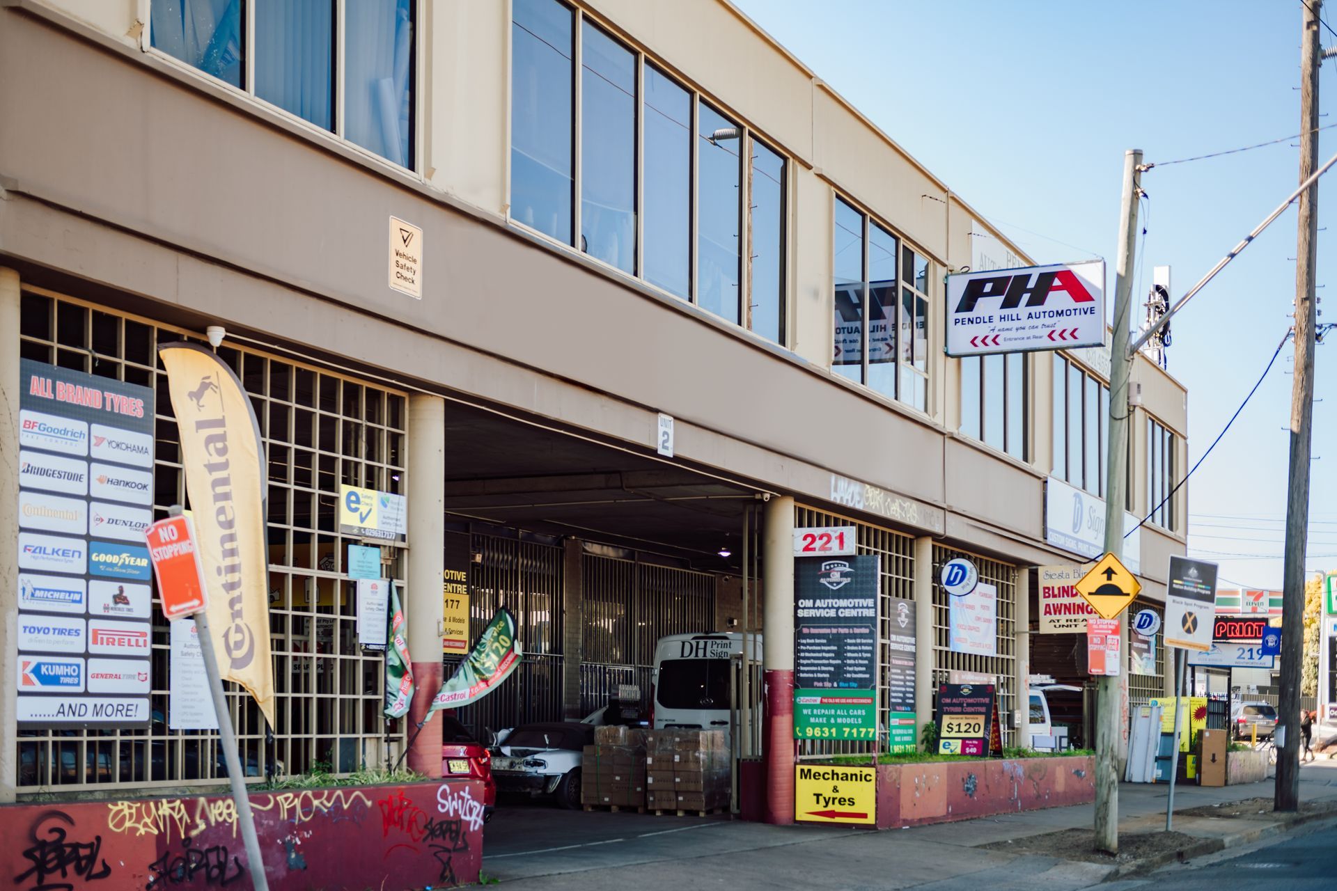 Exterior of a two-story auto shop with signs, cars, and Continental tire banner, along a street.