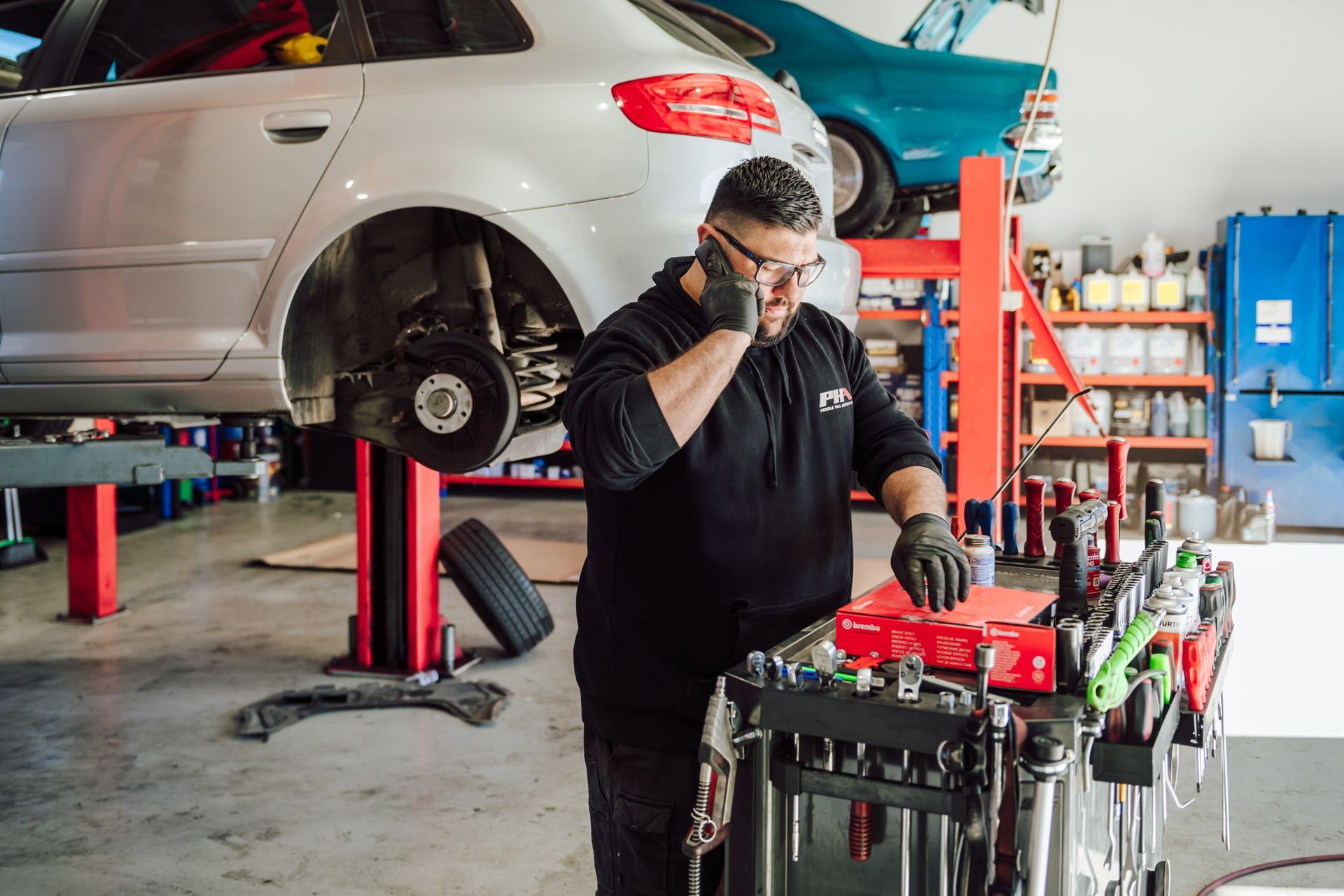 Mechanic on phone, working on a car lifted in a garage.