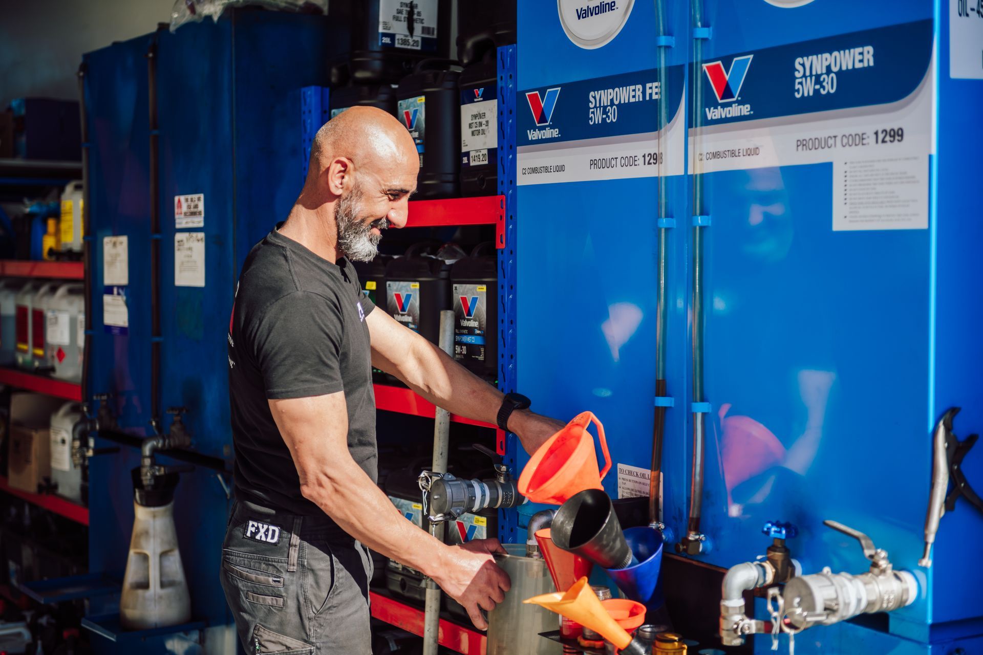 Bald man using a funnel to dispense fluid from a large blue tank.