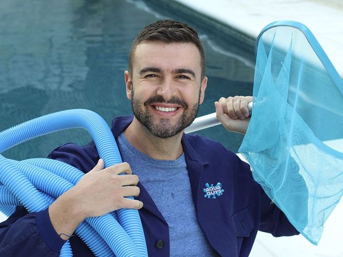 a man is holding a hose and a net in front of a swimming pool .