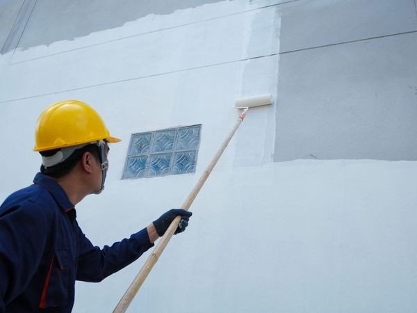 A man wearing a hard hat is painting a wall with a roller.