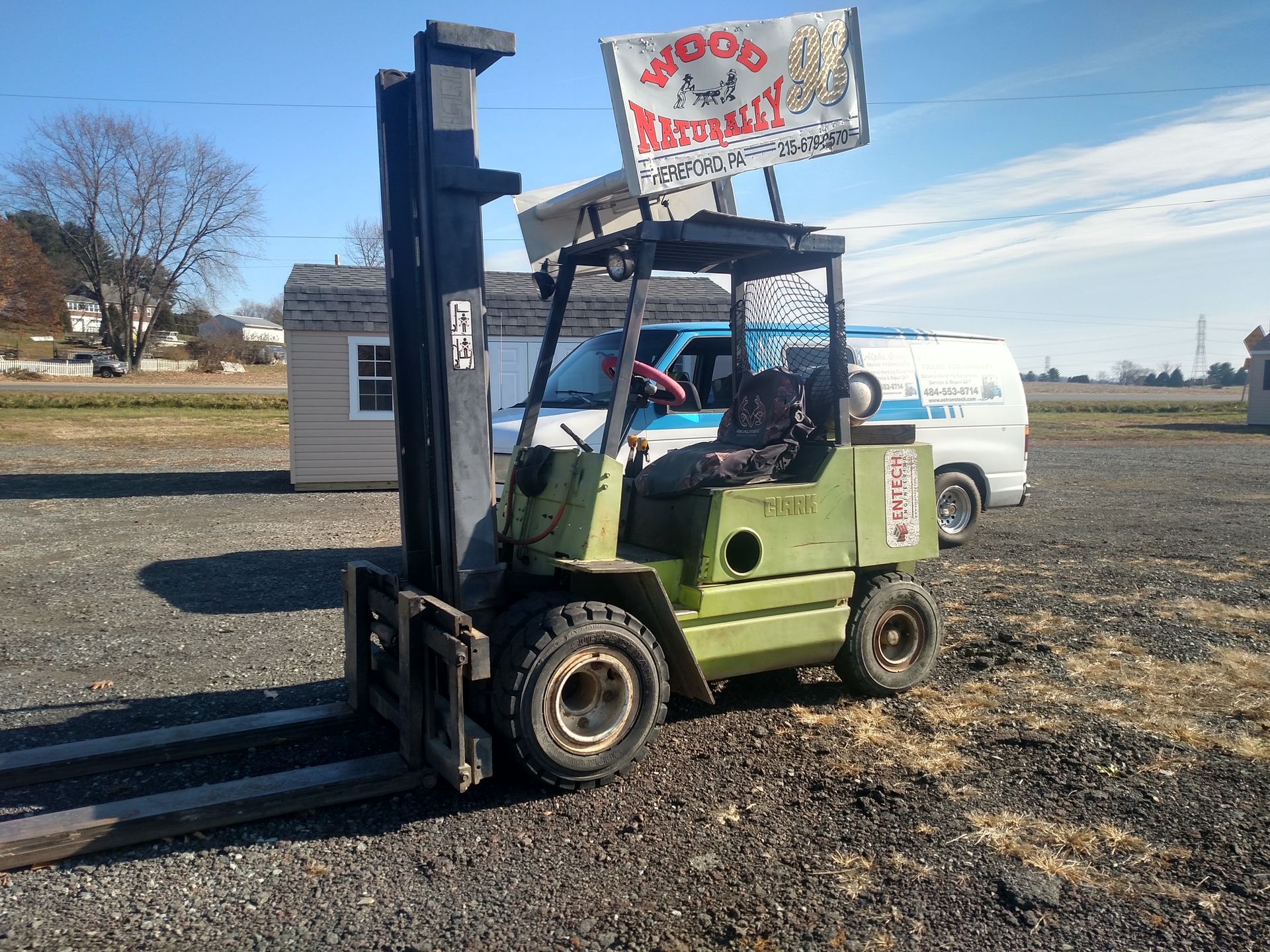 Forklift operator in orange suit carries a load on a street.