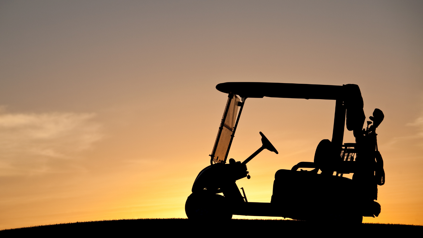Silhouette of a golf cart on a hill at sunset, with a warm orange sky in the background.