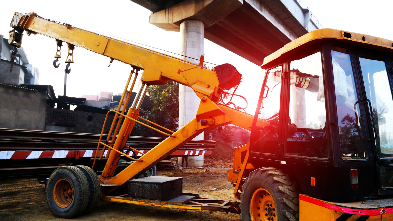 Yellow crane under an overpass, near construction site, with red-tinted sunlight.