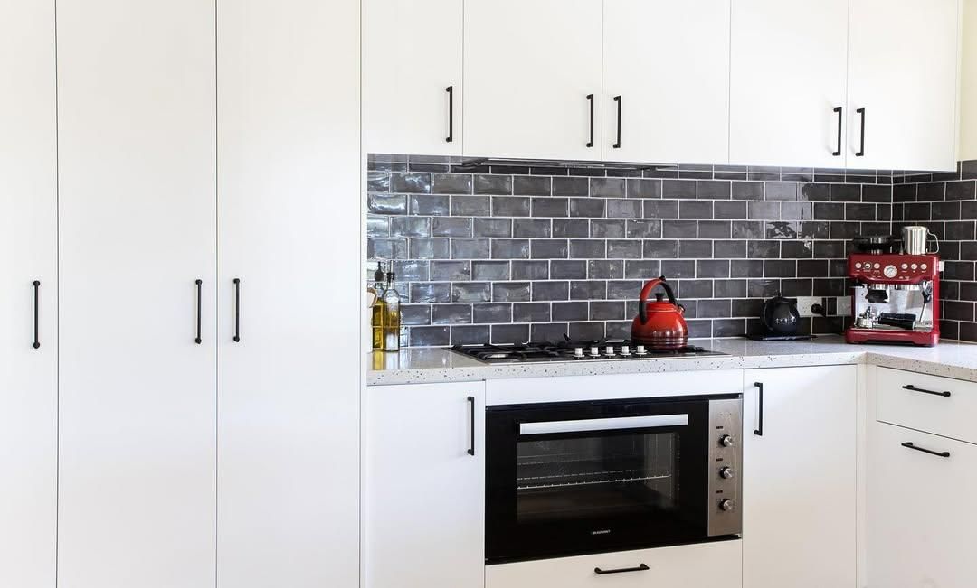 A Kitchen with White Cabinets and Black Appliances and A Brick Wall — Caldera Kitchens and Bathrooms in Lynchs Creek, NSW