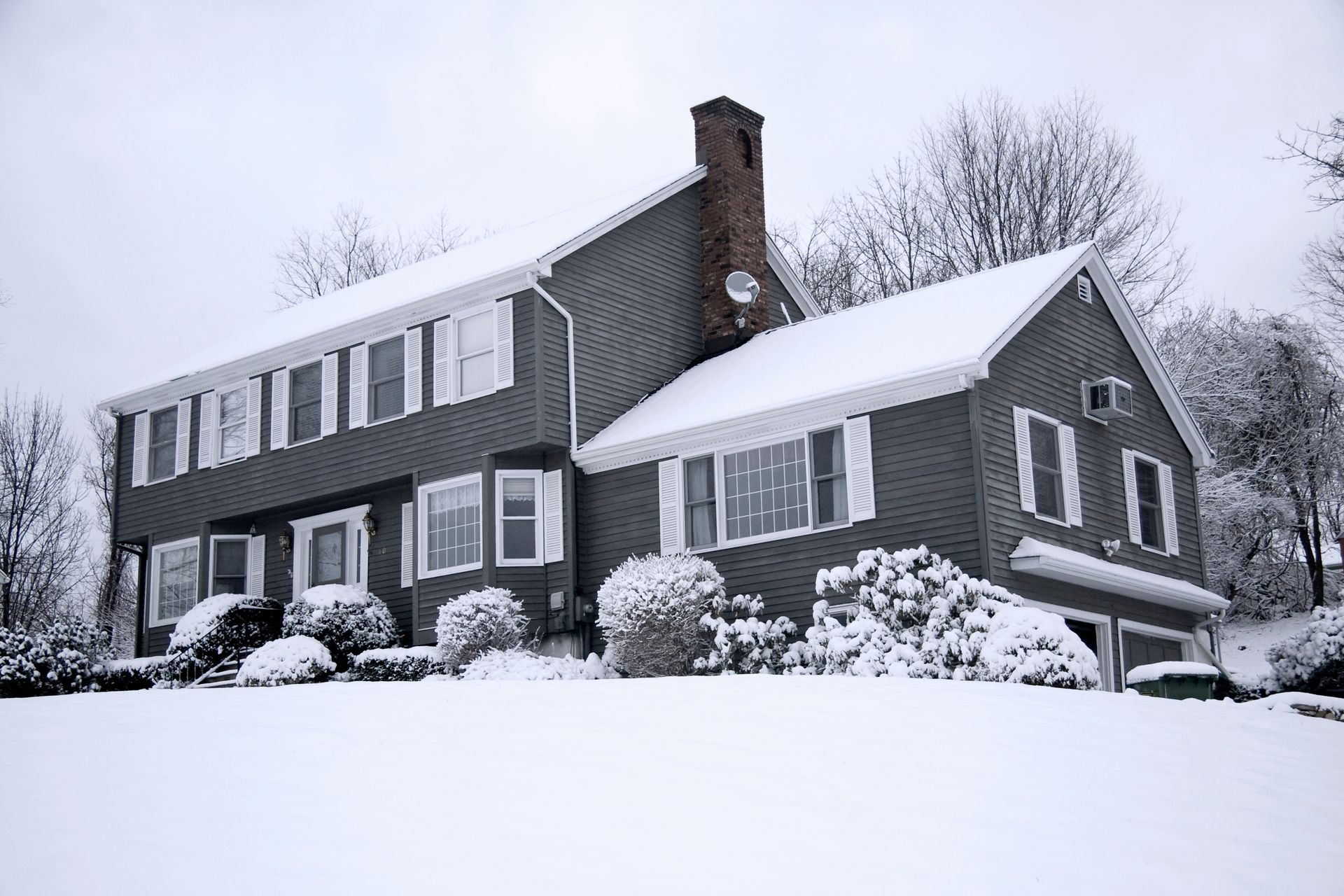 a gray house with white shutters is covered in snow