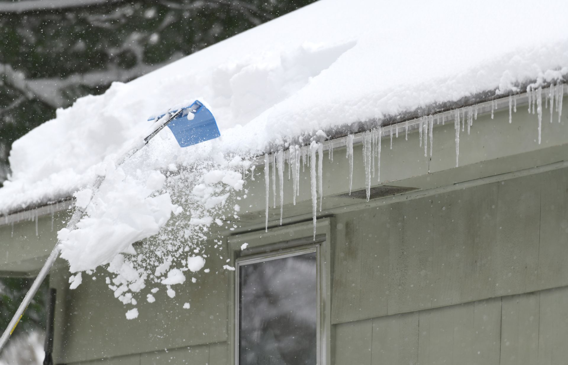 a person is clearing snow from the roof of a house using a roof rake in Western MA