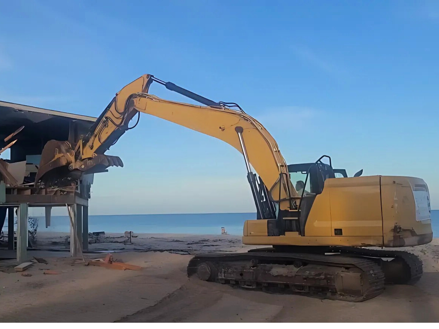 A coastal building demolition where an excavator is tearing down a beachfront property.