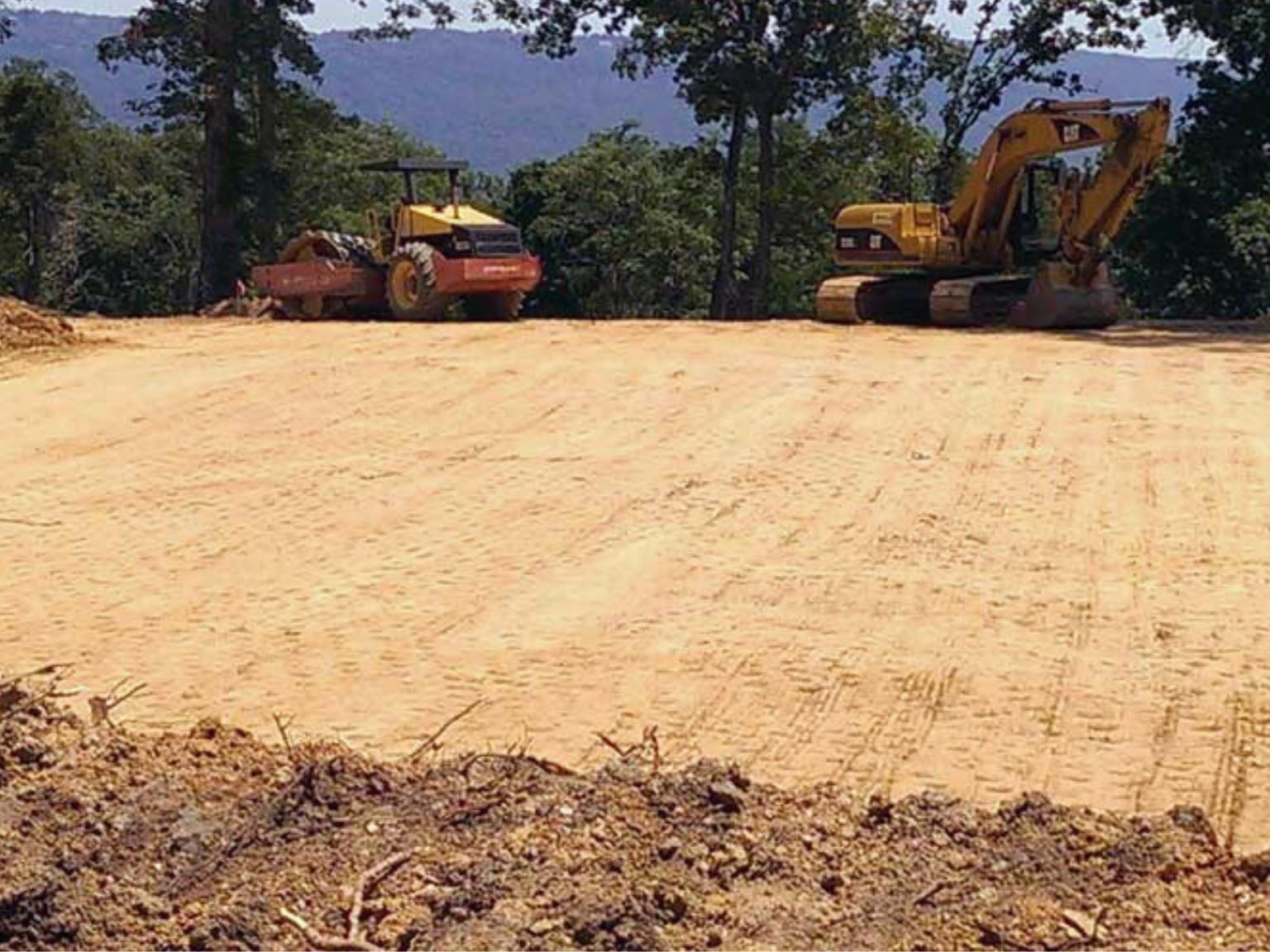 A freshly leveled and graded construction site surrounded by trees.