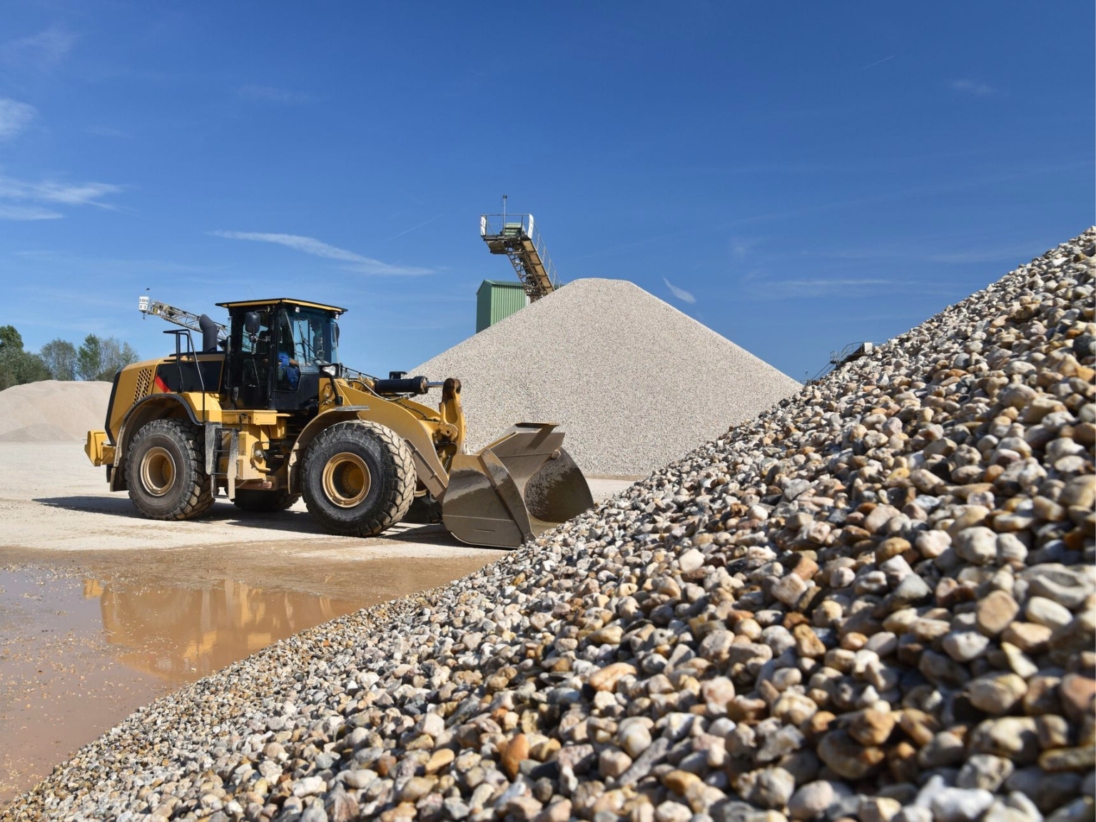 A large yellow front-end loader is parked near tall piles of crushed stone and gravel.