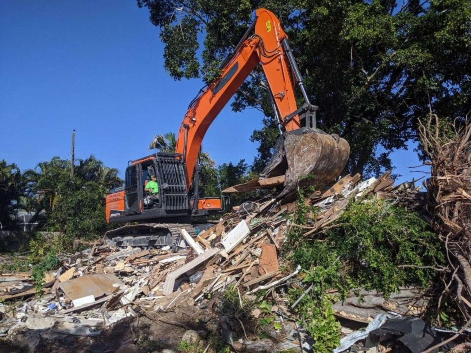 A demolition site wherean excavator is working atop a large pile of rubble.