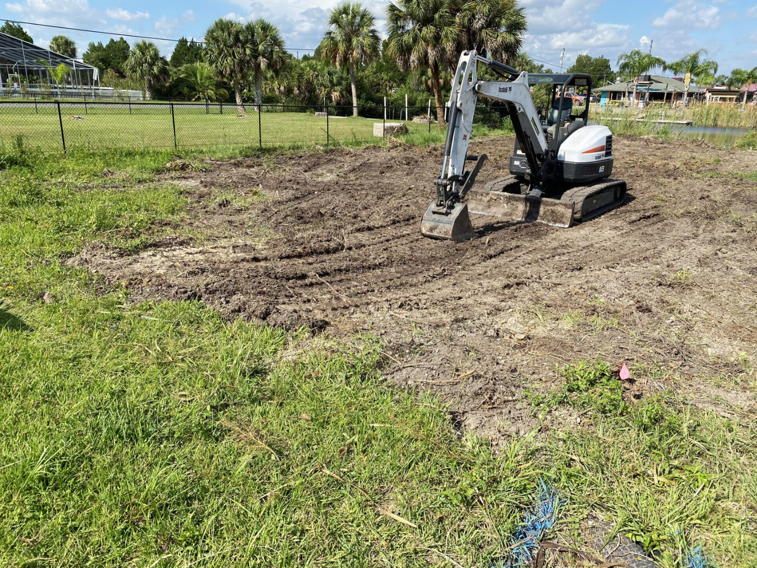 A compact Bobcat mini excavator is working on a residential lot with freshly disturbed soil in Port St. Lucie, FL.