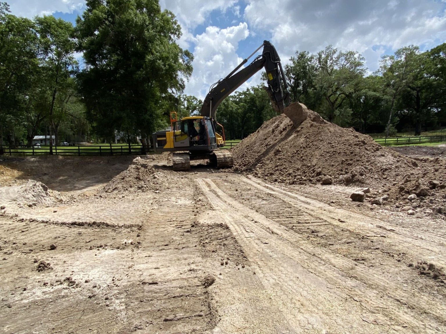 An excavator is working on a land grading project with trees in the back.