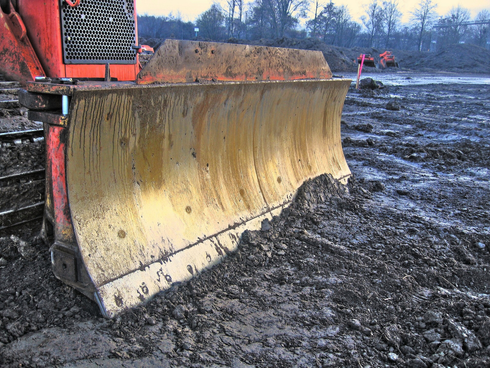 A close-up of a bulldozer blade working on a muddy construction site in Port St. Lucie, Florida.