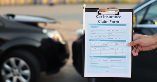 Person holding car insurance claim form near a damaged black car.