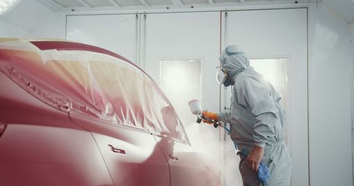 Person in protective suit painting a car red in a spray booth.