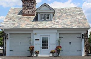 Front view of a white double garage with a shingled roof, central door, and flower pots by the entrance