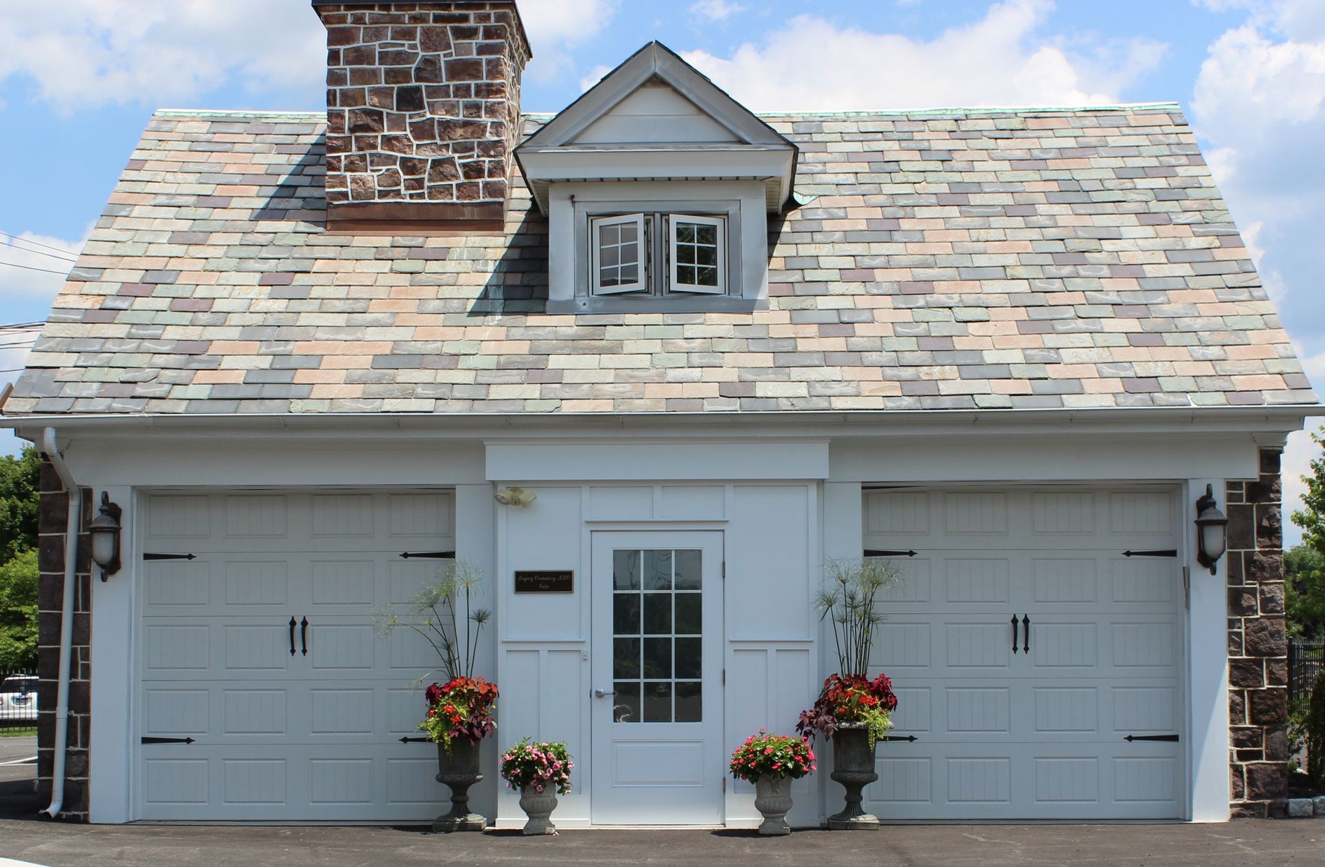 White garage with two doors, central entry, flower pots, and brick chimney under a shingled roof