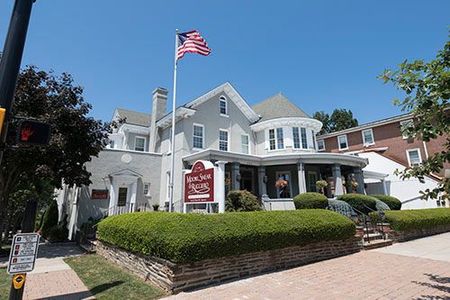 Historic white house with an American flag, porch, and sign under a bright blue sky