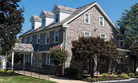 Stone house with a slate roof, white trim, and a landscaped front yard under a clear sky